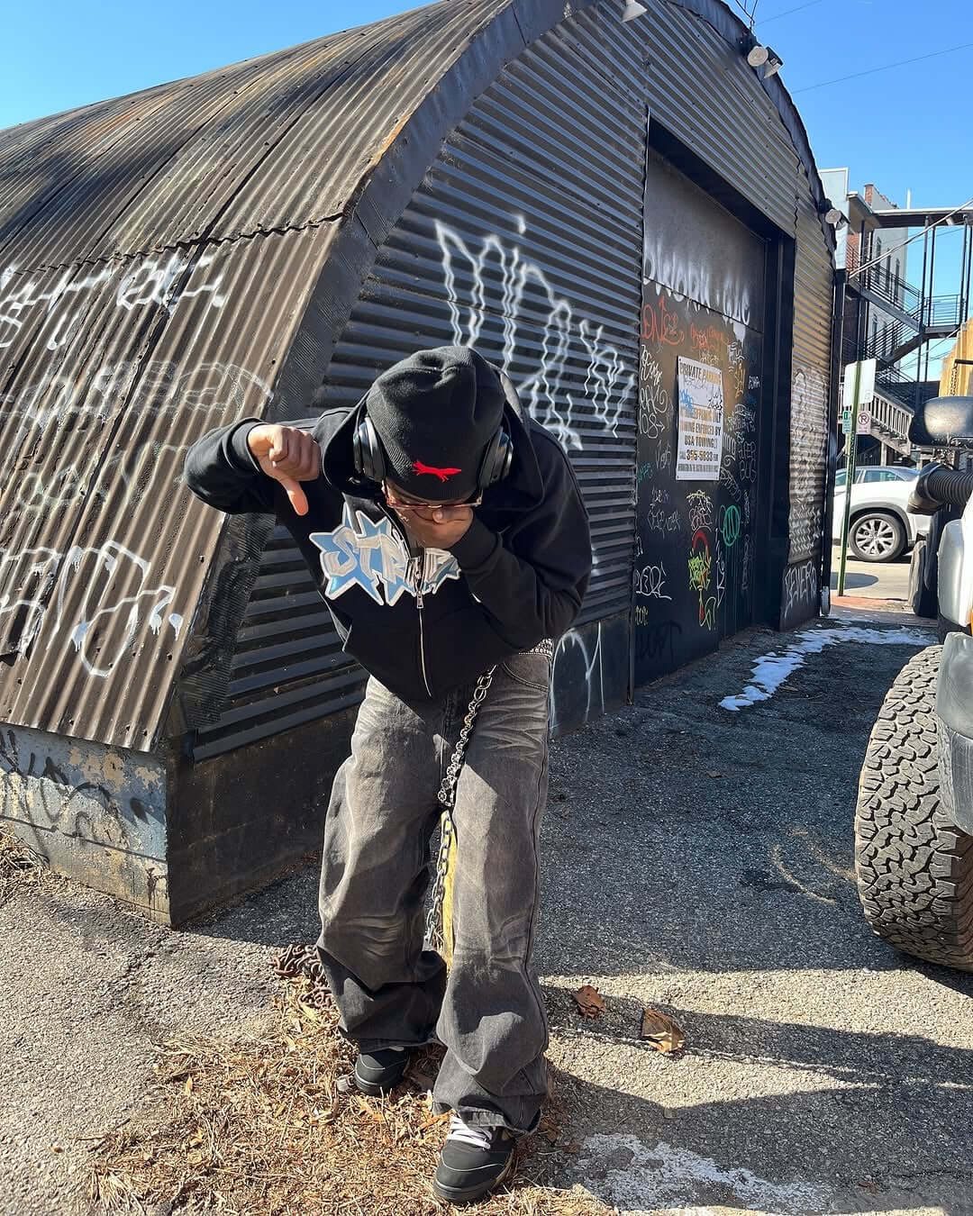 Person wearing BLACK GRAFFITI ZIP UP hoodie, posing against a graffiti-covered wall.